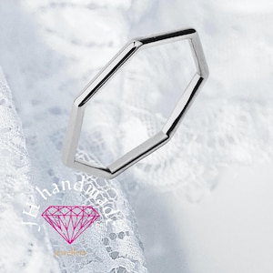 May include: A silver-colored, geometric ring with a hexagonal design. The ring is made of a shiny, reflective metal and is set against a white lace background. The ring is a piece of jewelry.