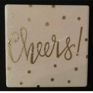 Può includere: Sottobicchiere bianco con glitter dorati e pois dorati. La parola "Cheers!" è scritta in corsivo dorato.