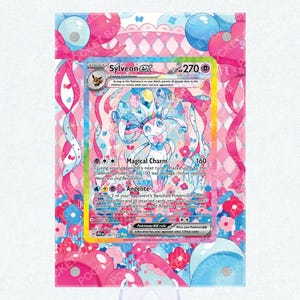 May include: A Sylveon EX Pokémon card with a pink and blue design, featuring the text "Sylveon EX" and "Magical Charm". The card is displayed on a white stand, with a Pocket Ranger Studio logo at the bottom.