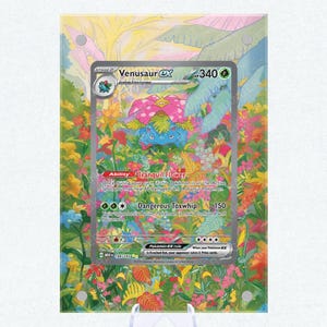 May include: A Pokémon trading card featuring Venusaur EX, with a vibrant floral background. The card displays the character's stats and abilities, including "Tranquil Flower" and "Dangerous Toxwhip". The card is displayed on a clear stand.