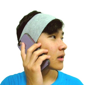 以下が含まれることがあります： グレーのヘッドバンドと青いTシャツを着た人が、紫色の携帯電話で話しています。