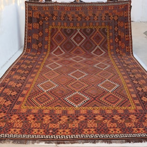 Puede incluir: Una alfombra rectangular grande con un patrón geométrico en tonos marrones, naranjas y rojos. El diseño central presenta formas de diamante, enmarcadas por bordes con patrones intrincados. La alfombra tiene un borde con flecos.