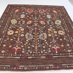 May include: A brown, rectangular rug with an intricate floral design. The rug features a central pattern of stylized flowers and branches in shades of red, blue, orange, and cream, set against a dark brown background. The border has a repeating pattern.