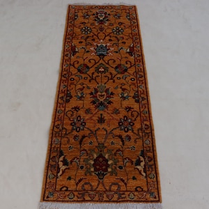 Könnte beinhalten: Ein orangefarbener Läuferteppich mit einem aufwendigen Blumenmuster in Rot, Blau und Grün. Der rechteckige Teppich hat unten eine Franse. Das Design zeigt detaillierte Blumenmotive und einen Rand. Ca. 200 cm lang.