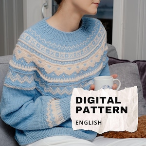 Könnte beinhalten: Hellblauer Strickpullover mit cremefarbenem geometrischen Muster an Passe und Ärmeln. Die Wörter "DIGITAL PATTERN" und "ENGLISH" sind auf einer Papierüberlagerung zu sehen. Der Pullover ist ein gemütliches, handgefertigtes Kleidungsstück.
