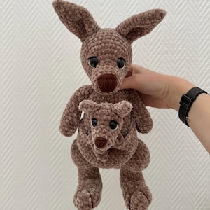 May include: A brown crocheted kangaroo plush toy holding a smaller brown crocheted kangaroo plush toy in its pouch.