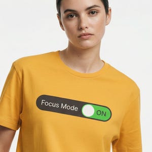 Könnte beinhalten: Senfgelbes T-Shirt mit einer Grafik eines Kippschalters mit der Aufschrift "Focus Mode" und dem Schalter in der Position "ON". Das Shirt hat kurze Ärmel und einen Rundhalsausschnitt.