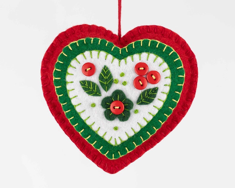 May include: A red felt heart ornament with green felt trim and white felt center. The center features a green felt flower with a red button center and green felt leaves with red button berries.