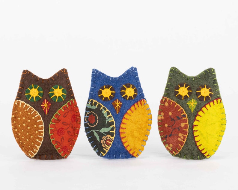 Embroidered felt owls with patterned wings in autumnal colours.