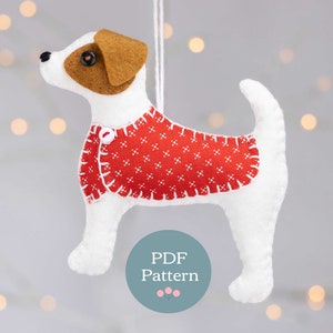 May include: White felt Jack Russell terrier dog ornament wearing a red and white patterned sweater. The ornament has a loop for hanging and says "PDF Pattern" on a teal circle.