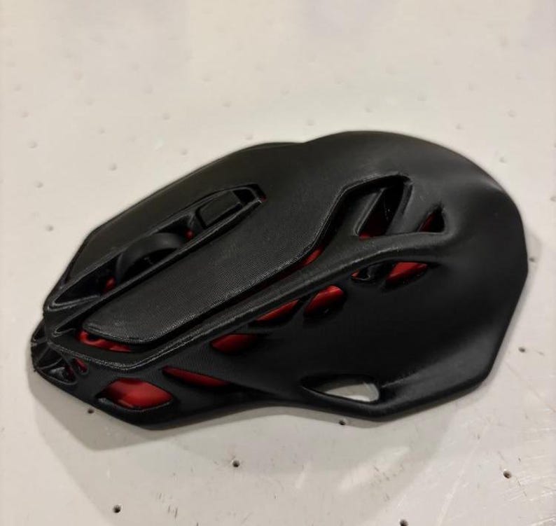 May include: A black computer mouse with a red, honeycomb-like design. The mouse has a scroll wheel and two buttons.
