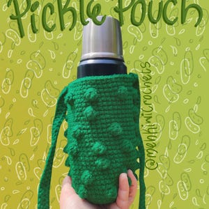 Op de afbeelding: Een groene gebreide komkommertas met een bruine band. De tas houdt een thermoskan van roestvrij staal vast. De tekst "Pickle Pouch" staat bovenaan de afbeelding in het zwart. De achtergrond is een groen patroon van komkommers.