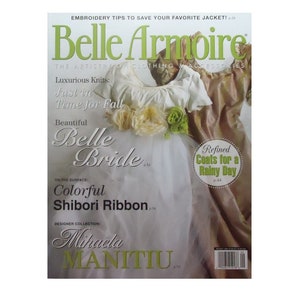 May include: A magazine cover featuring a young girl wearing a white dress with a pink and gold overlay. The magazine is titled "Belle Armoire" and features articles on luxurious knits, beautiful brides, and refined coats for a rainy day.