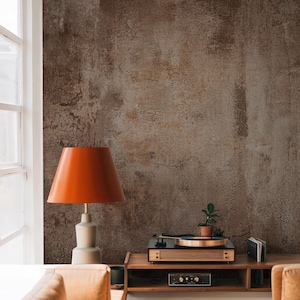 May include: An orange table lamp with a beige base and a gold accent sits next to a wooden record player. A small potted plant and a stack of records are also on the wooden shelf. The background is a textured brown wall.