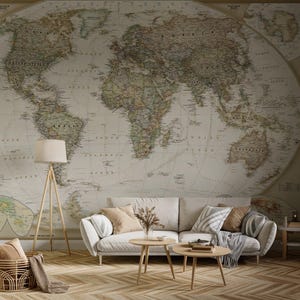 Peut inclure: Un salon avec une grande carte du monde murale. Un canapé blanc avec des coussins et une couverture est placé devant la carte. Deux petites tables basses en bois et un lampadaire complètent la décoration.