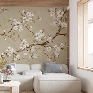 May include: A beige wall mural with a watercolour design of flowering branches with white blossoms and brown stems. The mural is behind a white sectional sofa with grey and patterned throw cushions. A wooden coffee table and window frame are also visible.