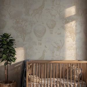 Op de afbeelding: Een kinderkamer met een licht houten bedje en behang met een safarithema. Het behang toont giraffen, olifanten en luchtballonnen in beige tinten. Het bedje heeft een kussen en deken met patronen. De kamer is verlicht door natuurlijk licht.