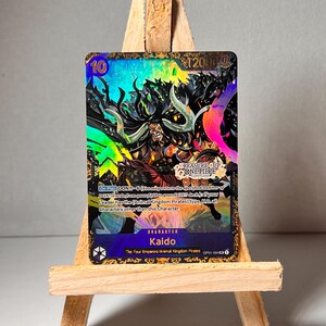May include: A collectible trading card featuring Kaido, a character from the anime and manga series One Piece. The card is holographic and features a colourful design with a black and white image of Kaido. The card has a power level of 12000 and a text description of Kaido's abilities.