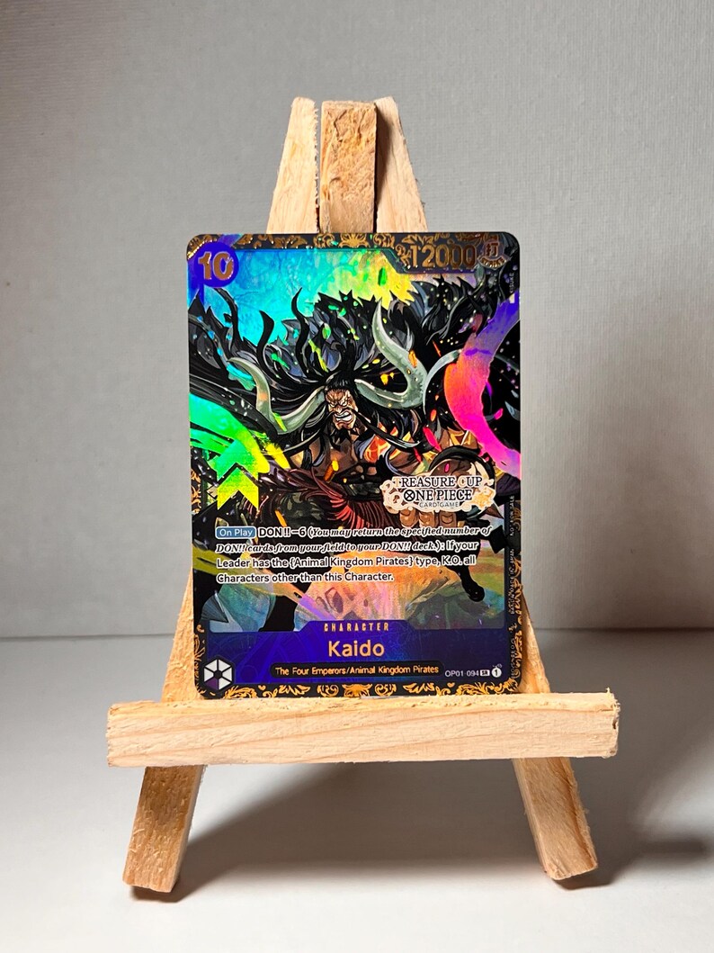 May include: A collectible trading card featuring Kaido, a character from the anime and manga series One Piece. The card is holographic and features a colourful design with a black and white image of Kaido. The card has a power level of 12000 and a text description of Kaido's abilities.