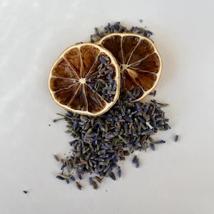 May include: Dried lavender buds and two dried lemon slices on a white surface.