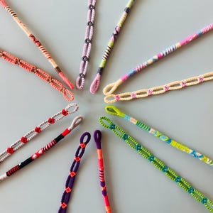 May include: A collection of 10 colorful friendship bracelets with various patterns and designs. The bracelets are made with colorful threads and have a variety of knots and braids.