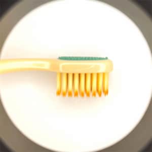 May include: A close-up of a yellow toothbrush with a green rubber grip and yellow bristles.