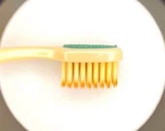 May include: A close-up of a yellow toothbrush with a green rubber grip and yellow bristles.