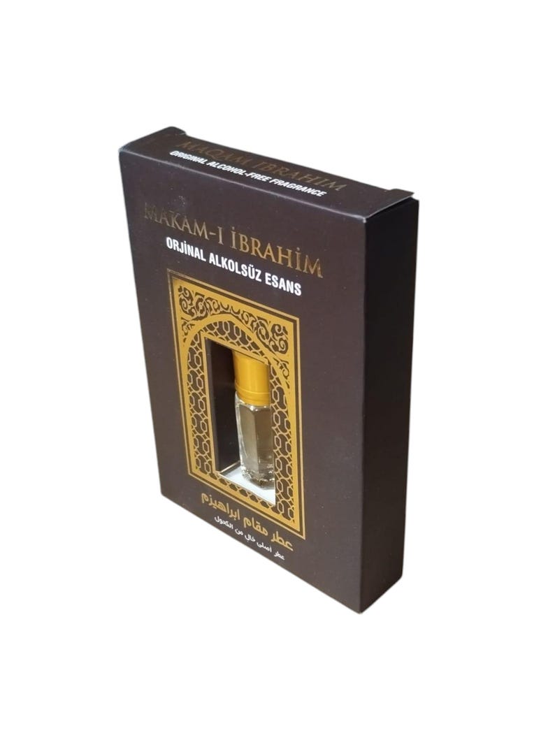 May include: A brown box with gold accents and a small clear glass bottle with a gold cap. The box has the text "MAKAM-I İBRAHİM" and "ORJİNAL ALKOLS&Uuml;Z ESANS" in gold lettering. The box also has the text "عطر مقام ابراهیزم" in Arabic script.