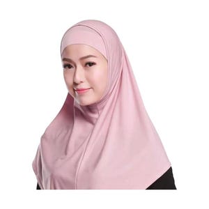 May include: A light pink hijab, a traditional head covering, is shown. The hijab is made of a soft, draping fabric and covers the head and neck. The design includes a separate cap that fits closely to the head.