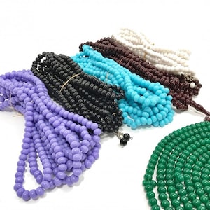 May include: A set of six prayer beads, or misbaha, in various colors, including purple, turquoise, black, brown, white, and green. The beads are made of a smooth, round material and are strung together on a thin cord.