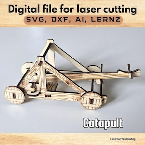 May include: A wooden catapult model, a digital file for laser cutting. The model features a detailed design with wheels and a launching arm. The text "Digital file for laser cutting" and "Catapult" are visible.