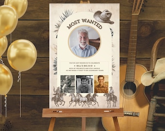 Op de afbeelding: Een verjaardagsbord met een western thema, met de tekst "Most Wanted" en "Bill's Big 8-0!". Het bord bevat een foto van een man en drie kleinere foto's. Het staat op een ezel, met gouden ballonnen en een gitaar op de achtergrond.