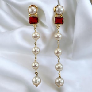 May include: A pair of long, gold earrings with red and white gemstones and a pearl drop design.