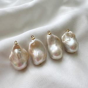 以下が含まれることがあります： 虹色に輝く白とクリーム色の表面を持つ4つの不規則なバロックパール。それぞれの上部には吊り下げ用の小さな金色の金属製ベイルが付いています。真珠は独特の有機的な形状をしており、滑らかで光沢のある質感とほのかなピンクの色合いが特徴です。
