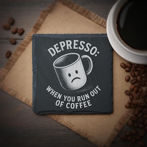 Op de afbeelding: Een vierkante, donkergrijze leistenen onderzetter met de tekst "Depresso: When you run out of coffee" en een afbeelding van een verdrietige koffiemok. De onderzetter ligt op een beige jute placemat, met een kopje koffie en koffiebonen in de buurt.