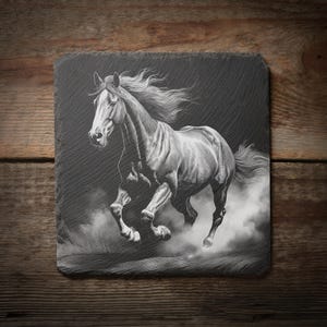 May include: A black and white image of a running horse etched on a square slate coaster. The horse is depicted in motion, with its mane and tail flowing. The coaster is set against a wooden background.