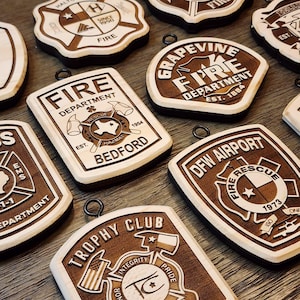 May include: Wooden fire department and trophy club ornaments with various designs and text. The ornaments are brown with light wood accents and include the text "Fire Department", "Rescue", and "Trophy Club".