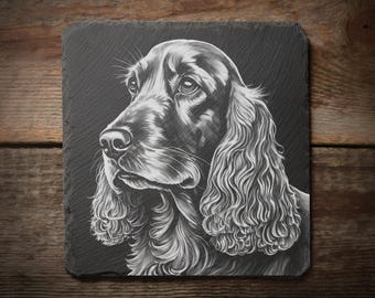 May include: A black slate coaster featuring a detailed, grayscale portrait of a Cocker Spaniel dog. The dog's fur is meticulously rendered, highlighting its long, flowing ears and expressive eyes. The coaster is square and rests on a wooden surface.
