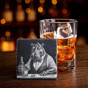 Può includere: Un sottobicchiere in ardesia nera con un'illustrazione dettagliata di un ippopotamo vestito da barista, che tiene in mano una bottiglia e un bicchiere. Un bicchiere di whisky con ghiaccio è accanto al sottobicchiere.