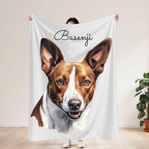 May include: White blanket featuring a Basenji dog portrait. The dog has brown and white fur, with large, upright ears and a friendly expression. The word "Basenji" is written in cursive at the top of the blanket.