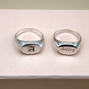 Puede incluir: Dos anillos de sello de plata. El anillo de la izquierda est&aacute; grabado con la letra "A". El anillo de la derecha est&aacute; grabado con el nombre "Ashley".