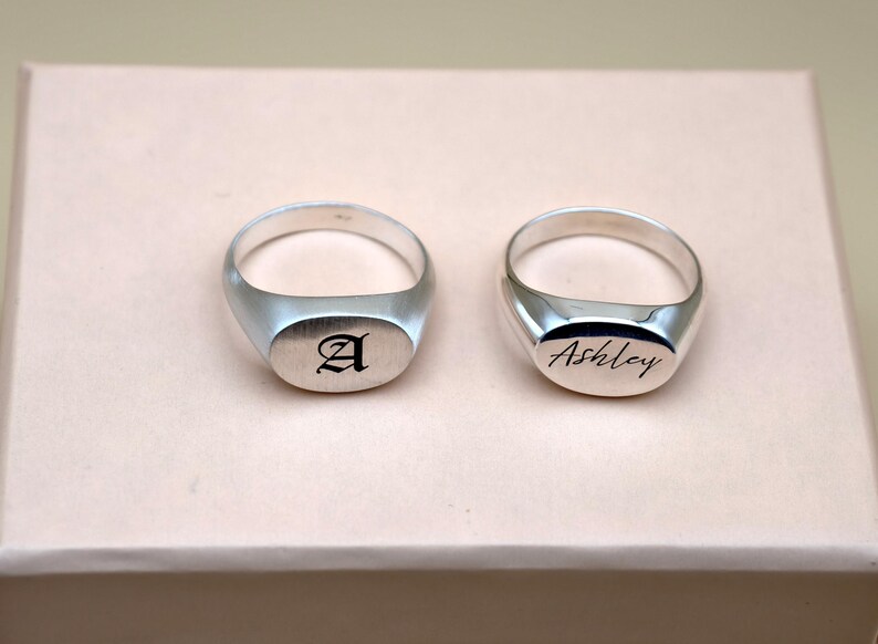 Puede incluir: Dos anillos de sello de plata. El anillo de la izquierda est&aacute; grabado con la letra "A". El anillo de la derecha est&aacute; grabado con el nombre "Ashley".