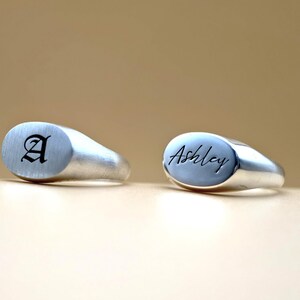 Puede incluir: Dos anillos de sello de plata con tapas ovaladas. Un anillo est&aacute; grabado con la letra "A" en fuente g&oacute;tica. El otro anillo est&aacute; grabado con el nombre "Ashley" en cursiva.