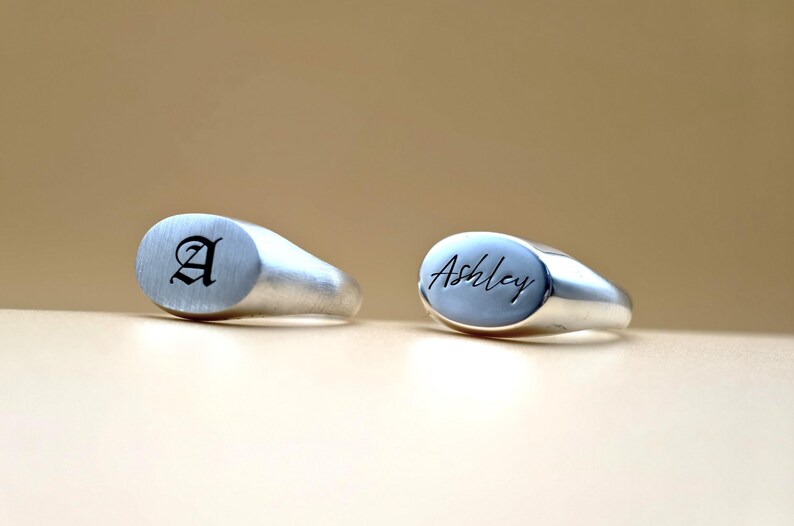 Puede incluir: Dos anillos de sello de plata con tapas ovaladas. Un anillo est&aacute; grabado con la letra "A" en fuente g&oacute;tica. El otro anillo est&aacute; grabado con el nombre "Ashley" en cursiva.