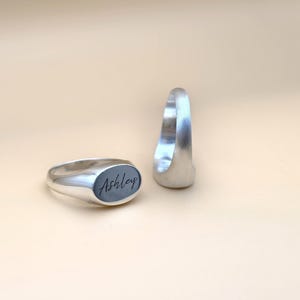 Puede incluir: Dos anillos de sello de plata, uno con el nombre "Ashley" grabado en la parte superior.