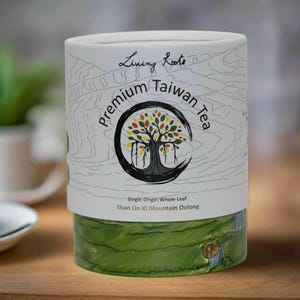 May include: A white cylindrical container with a green and white design. The container has the text "Living Roots Premium Taiwan Tea" and "Single Origin Whole Leaf Shan Lin Xi Mountain Oolong" printed on it.