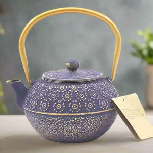 May include: Purple cast iron teapot with a gold handle and a floral design. The teapot has a lid with a knob on top.