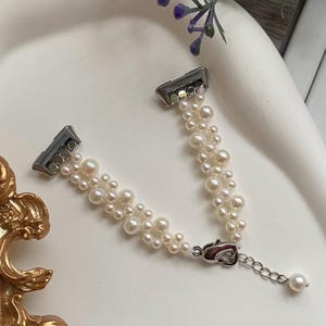 以下が含まれることがあります： シルバーの留め金とチェーンが付いた繊細なパールブレスレット。ブレスレットは、小さくクリーミーな白い真珠の複数のストランドで構成されており、テクスチャード加工でエレガントな外観を作り出しています。留め金とチェーンがデザインに輝きを添えています。