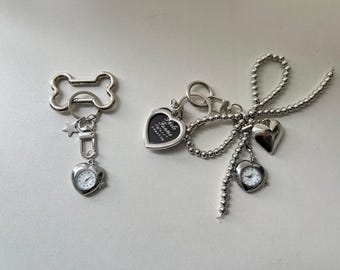 May include: Two silver keychains with charms. One keychain has a bone-shaped ring with a star and a small watch with a silver heart-shaped case. The other keychain has a silver heart-shaped photo frame with the text "Photo Frame" and a silver heart-shaped watch with a silver chain.