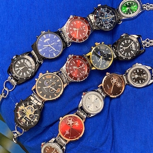 May include: An assortment of wristwatches with various face designs and band styles. The watches feature black, red, blue, and gold faces, with silver and black bands. Some watches have a chain-link style band. The background is a solid blue.